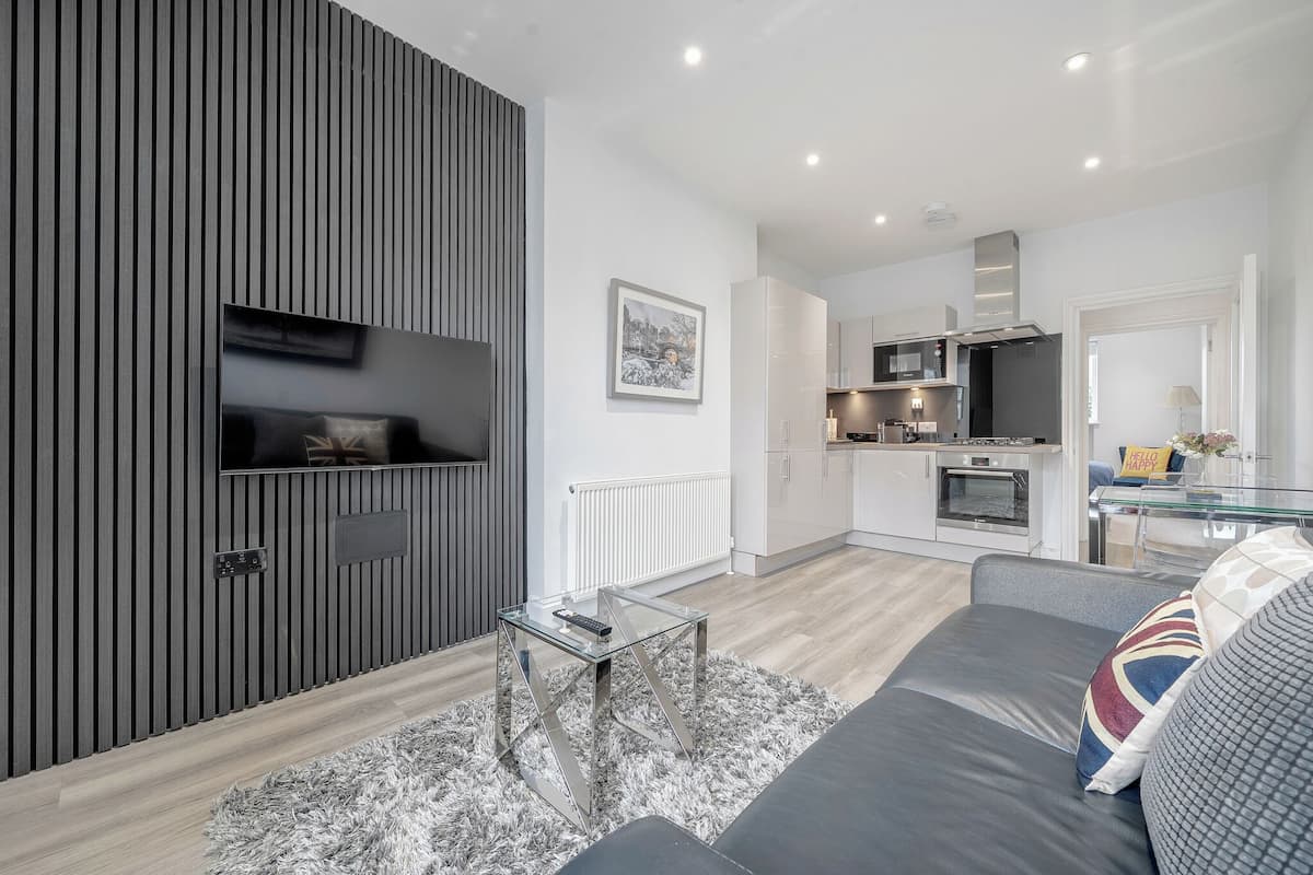 Una sala moderna con un sofá gris, una mesa de centro de vidrio y un televisor montado en una pared de paneles de madera.