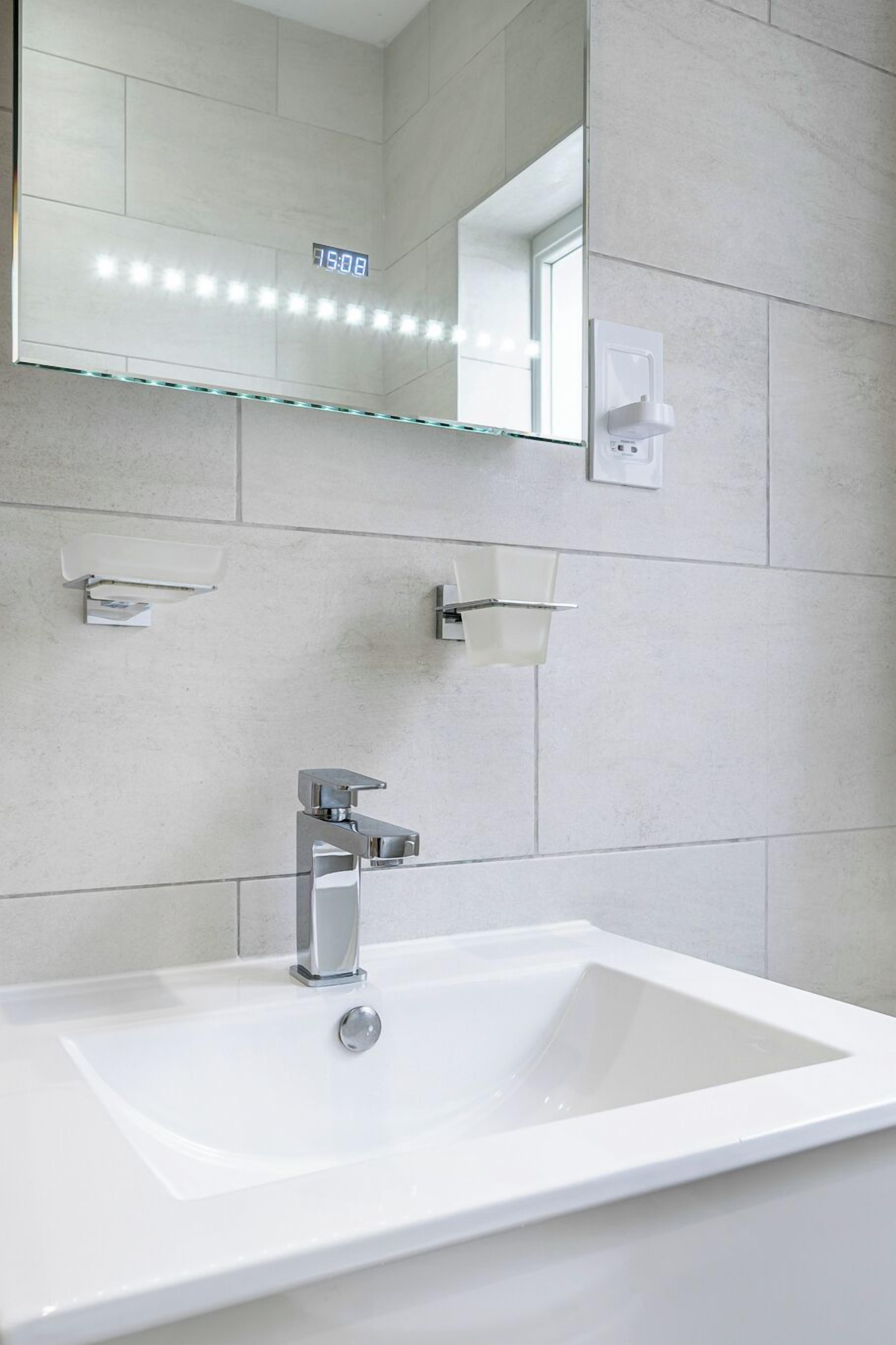 A modern bathroom with a white sink, chrome faucet, and a glass shelf above the mirror.