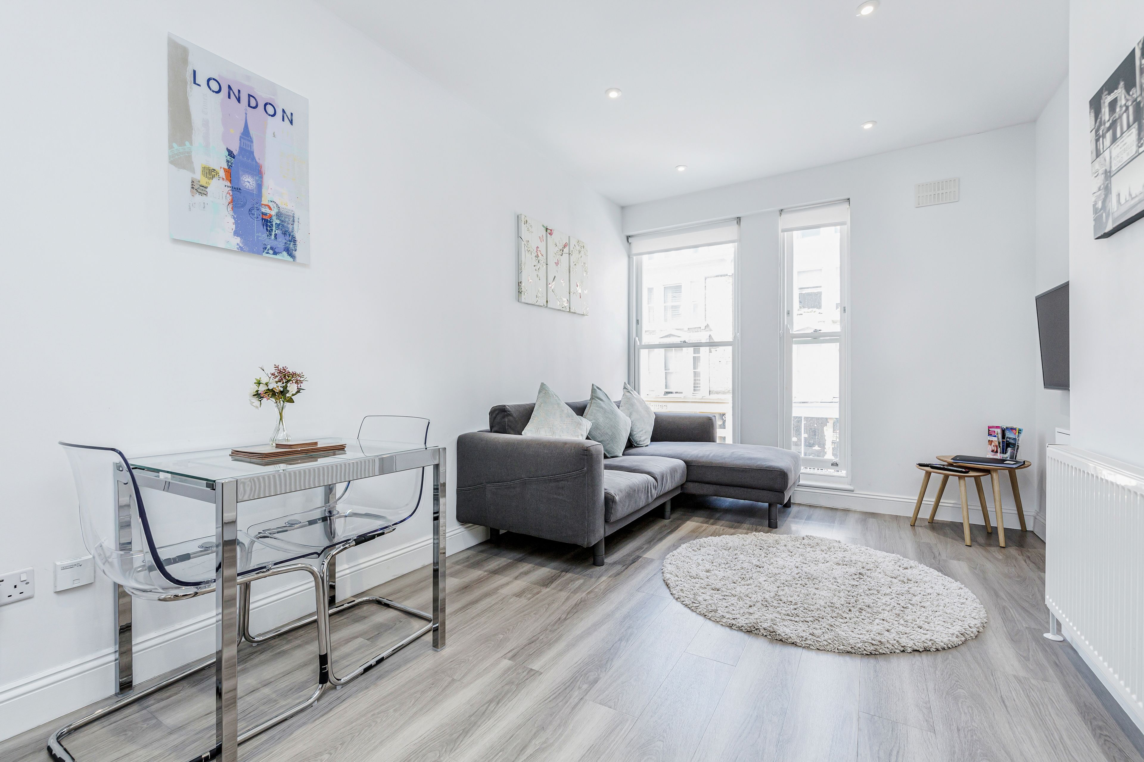 A modern living room with a grey sofa, a glass dining table, and a round rug.