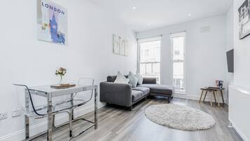 A modern living room with a grey sofa, a glass dining table, and a round rug.
