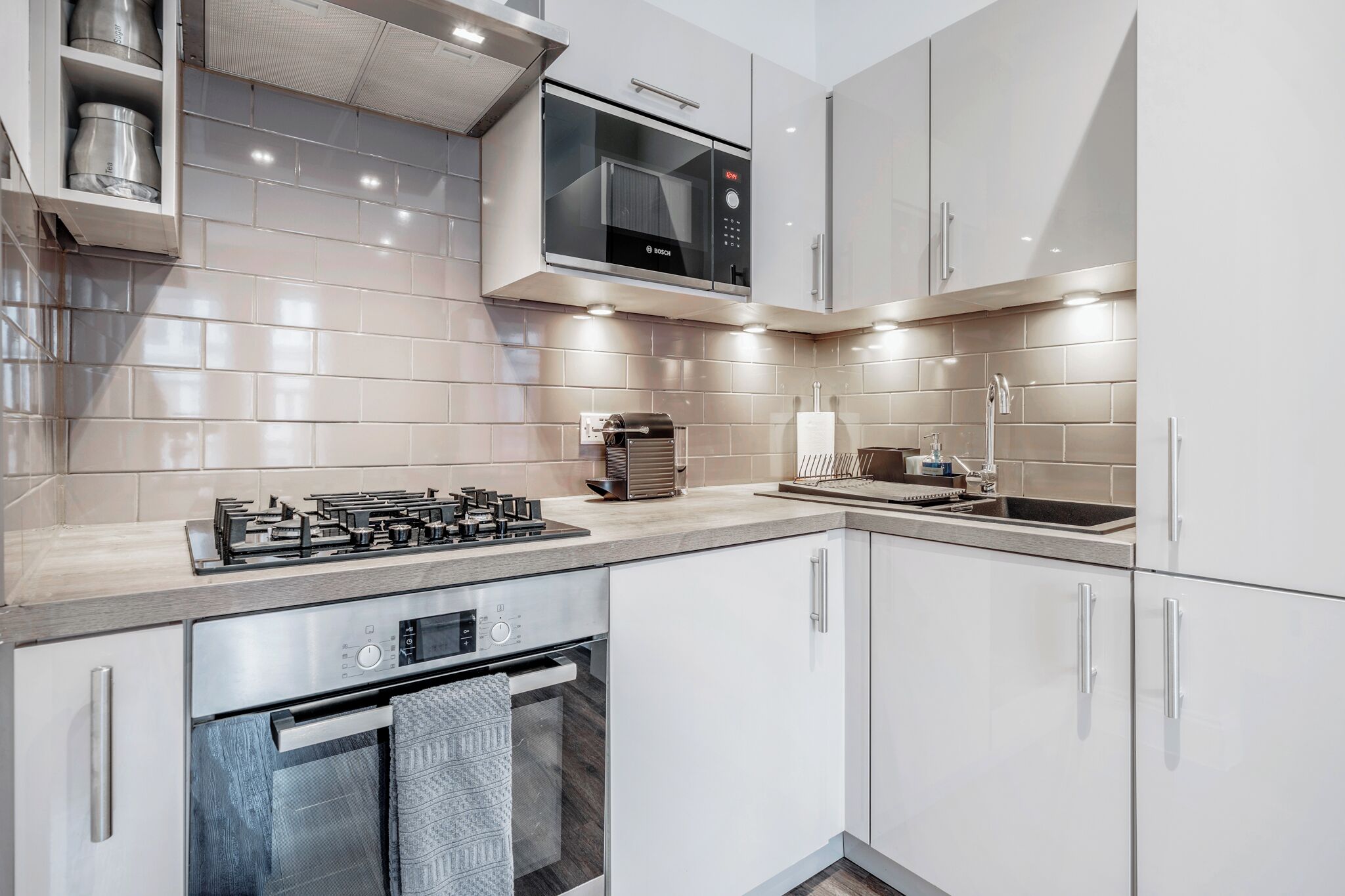 A modern kitchen with stainless steel appliances, white cabinetry, and a tiled backsplash.