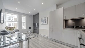 A modern kitchen with a glass dining table, white cabinets, and a large window. - 2 Bedroom Portobello Notting Hill Apartment (London)