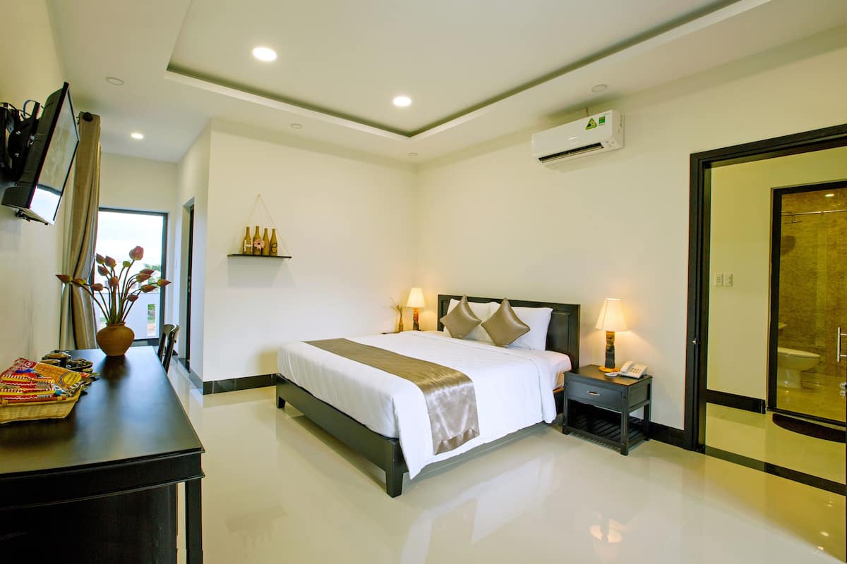 A modern hotel room with a large bed, bedside lamps, a small table with a phone, and a wall-mounted TV.