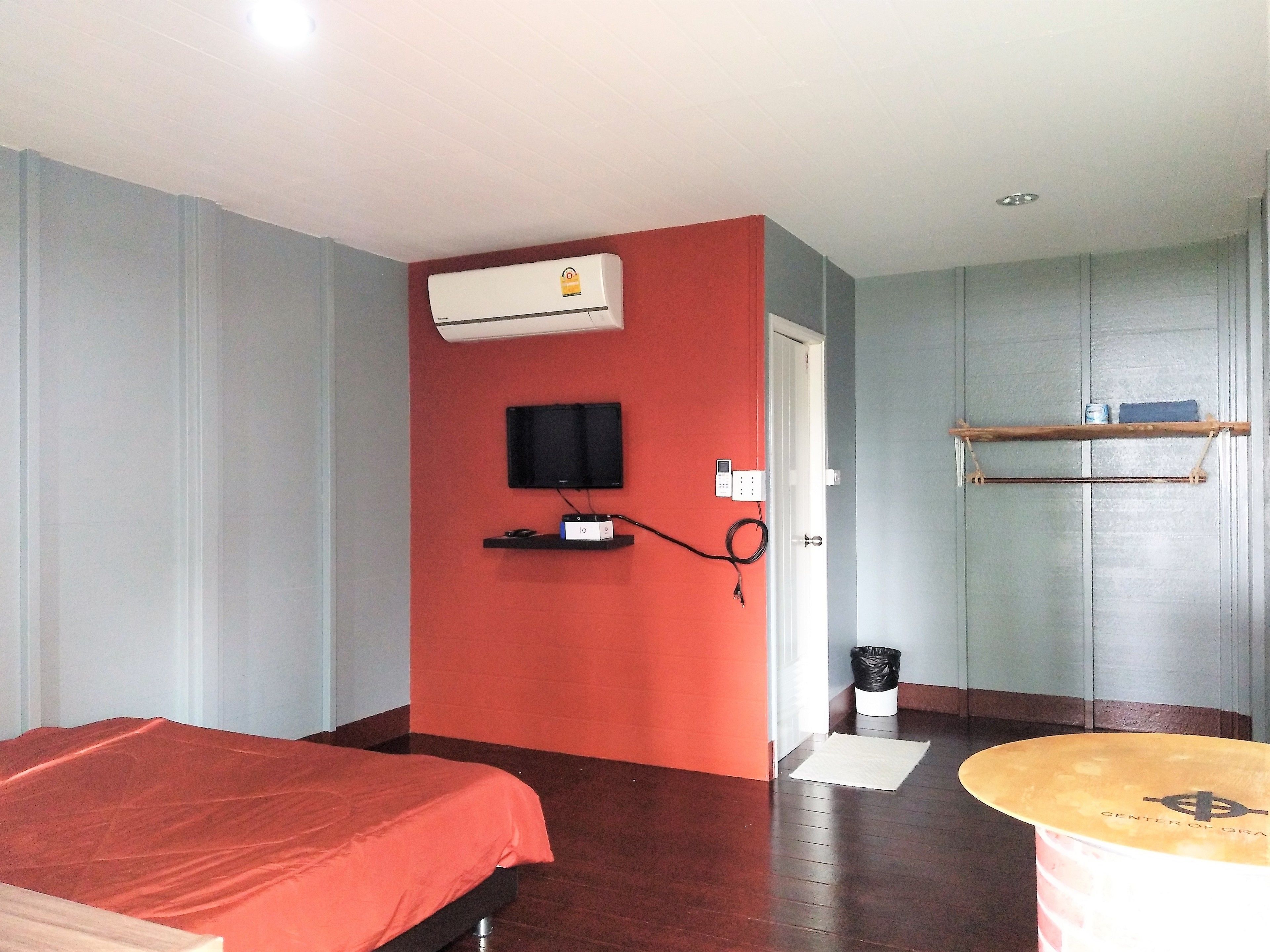 Habitación de hotel con cama, televisor, equipo de aire acondicionado, estante pequeño y puerta que da a otra habitación.