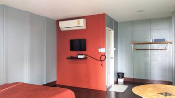 Habitación de hotel con cama, televisor, equipo de aire acondicionado, estante pequeño y puerta que da a otra habitación.