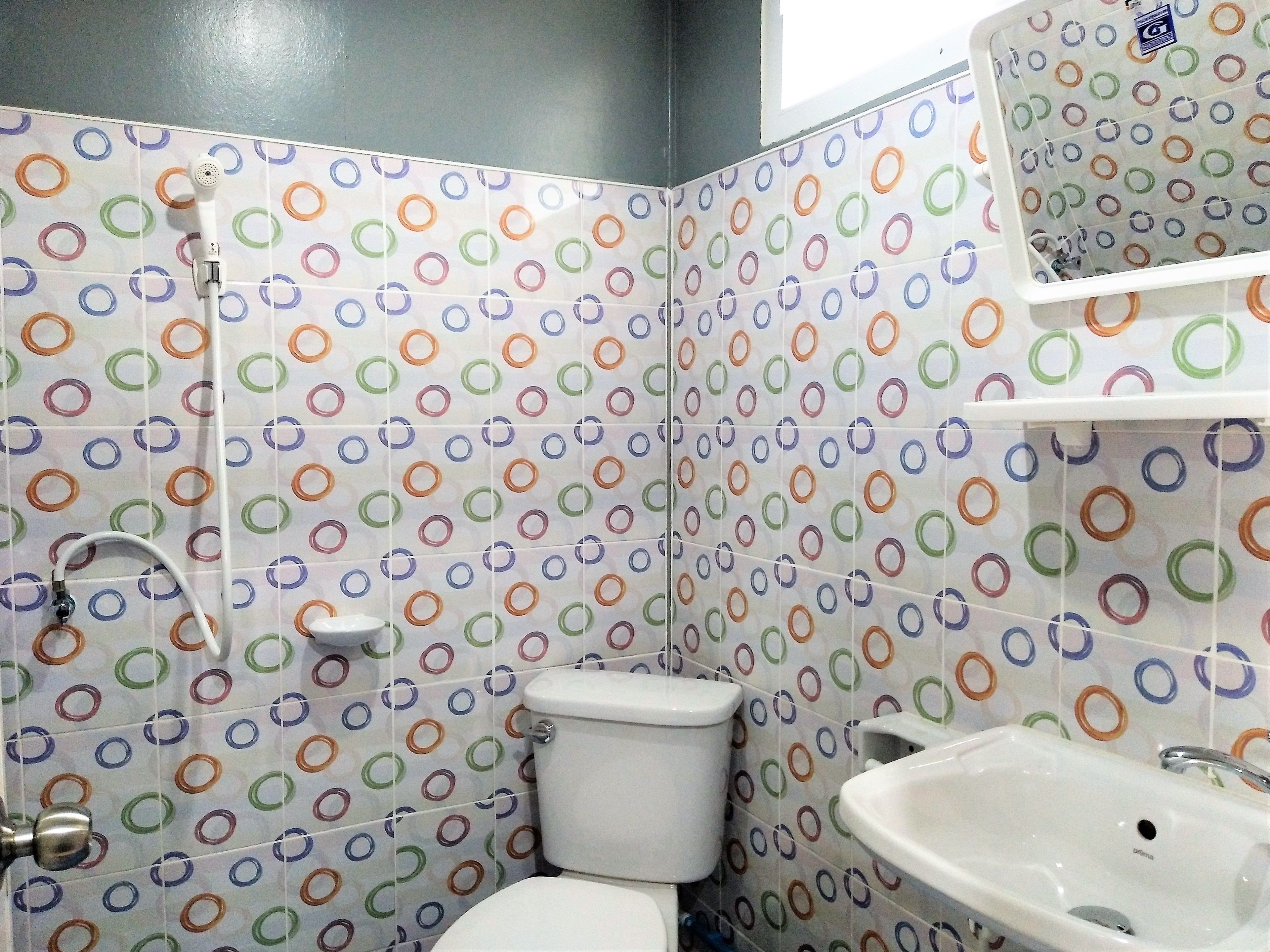 Een badkamer met toilet, wastafel en douche. De wanden zijn betegeld met een kleurrijk, cirkelvormig patroon.