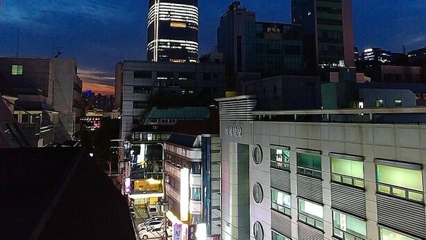 A cityscape at dusk with a prominent skyscraper illuminated at the center. - LotteTower Rainbow House (Seoul)