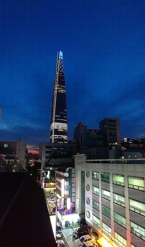 A cityscape at dusk with a prominent skyscraper illuminated at the center. - LotteTower Rainbow House (Seoul)