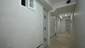 A hallway with white tiled walls, checkered door designs, and a light wooden floor. - LotteTower Rainbow House (Seoul)