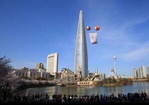 A tall skyscraper with a pointed top, surrounded by other buildings and a body of water.