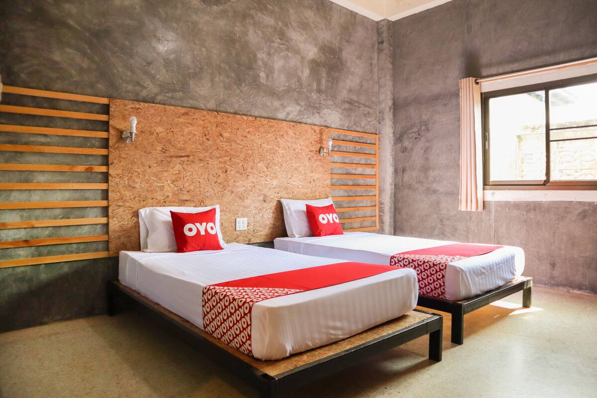 Une chambre d’hôtel avec deux lits, chacun doté d’une tête de lit en bois et de linge de lit blanc agrémenté de touches de rouge.