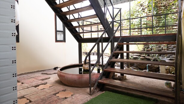 A staircase leading to a rooftop garden with a water feature and a stone wall. - OYO 674 Greenery Home (Ranong)