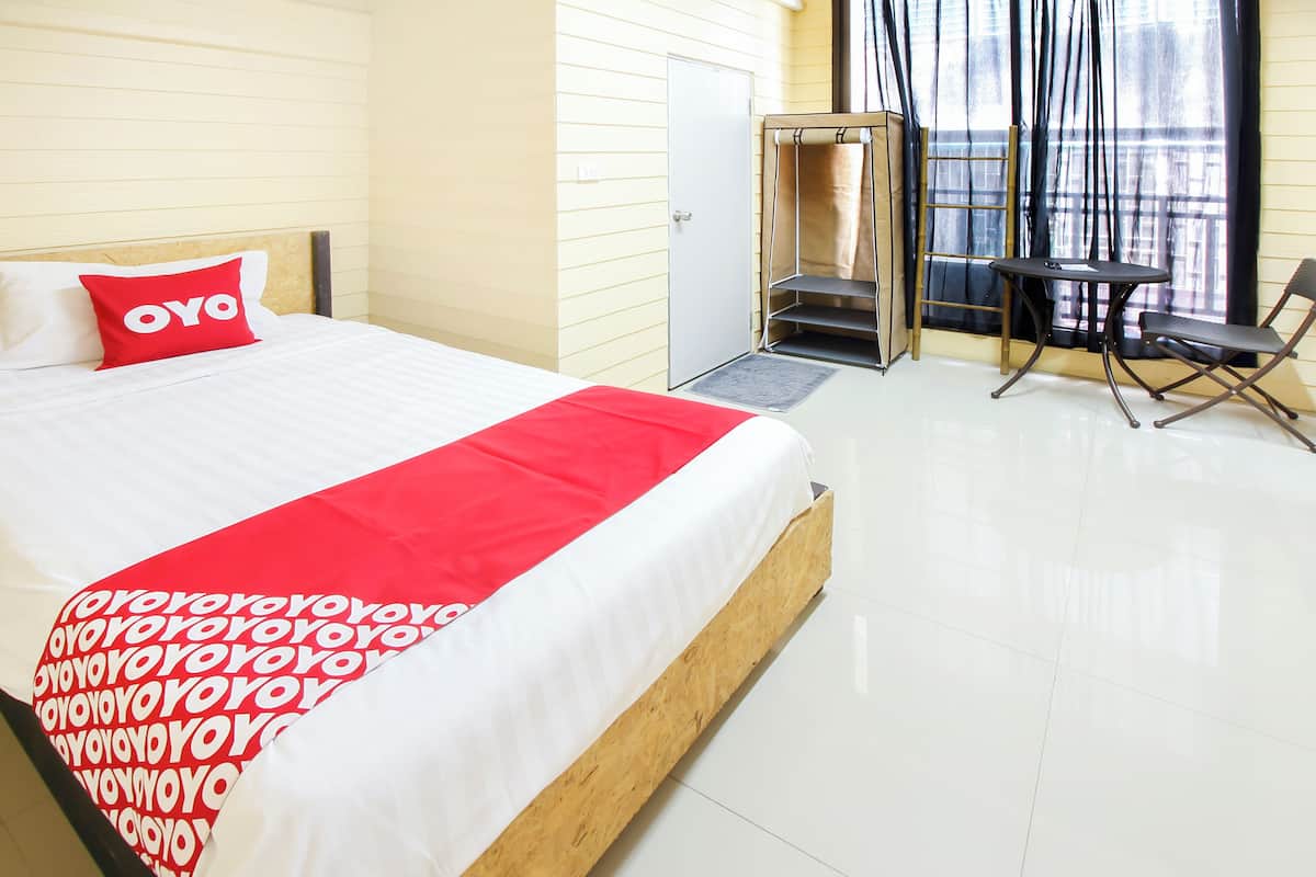 Une chambre d’hôtel avec un lit, une couverture rouge et blanche, une petite table, une chaise et une fenêtre avec des rideaux.