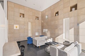 Un vestíbulo moderno con un sofá, sillas, una mesa y un cubo de basura azul.