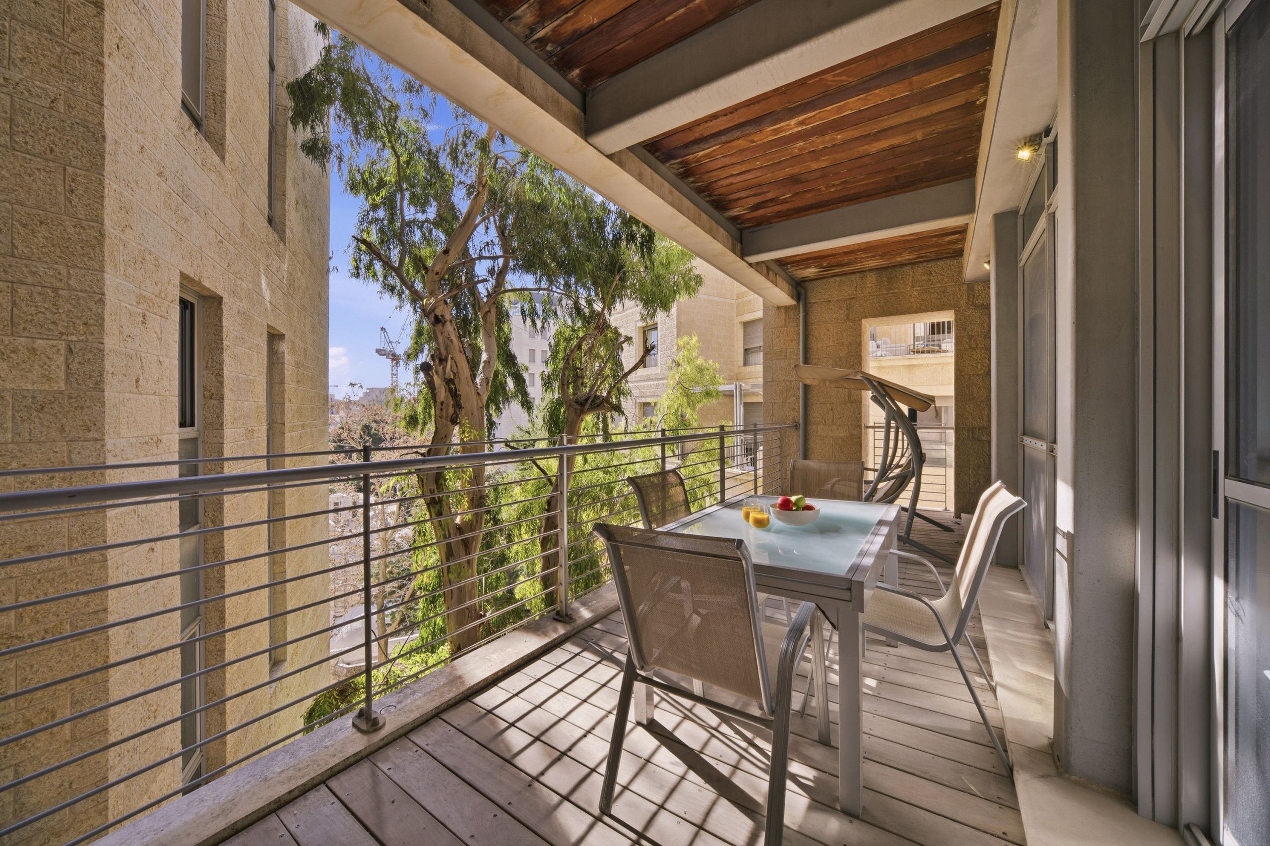 A balcony with a table and chairs, overlooking a courtyard with trees and buildings.