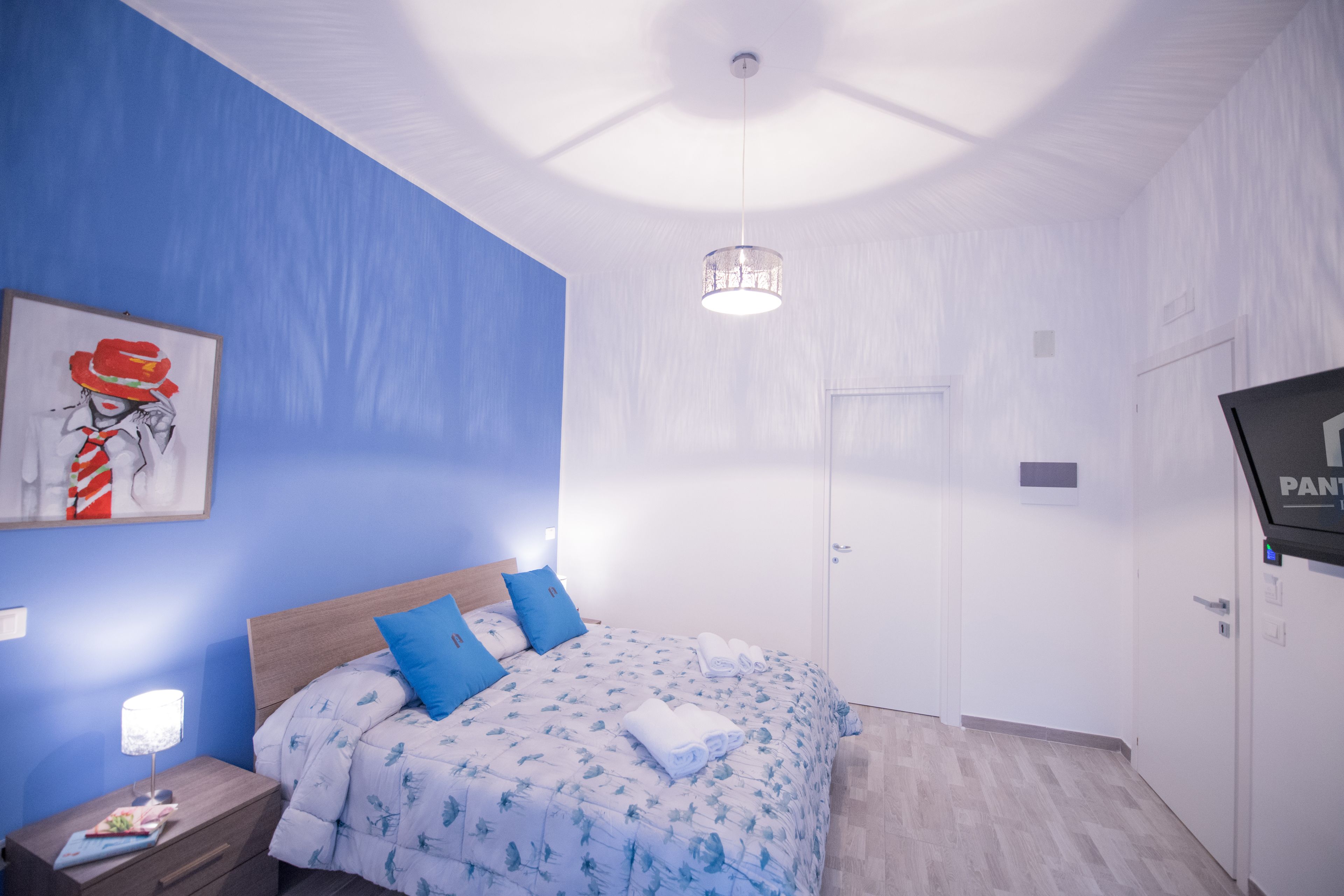 Une chambre à coucher comprenant un lit, une table de chevet, un téléviseur fixé au mur et un luminaire au plafond.
