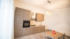 A modern kitchen with wooden cabinets, a gas stove, and a dining area with a table and chairs. - Panta Rei B&B (Salerno)