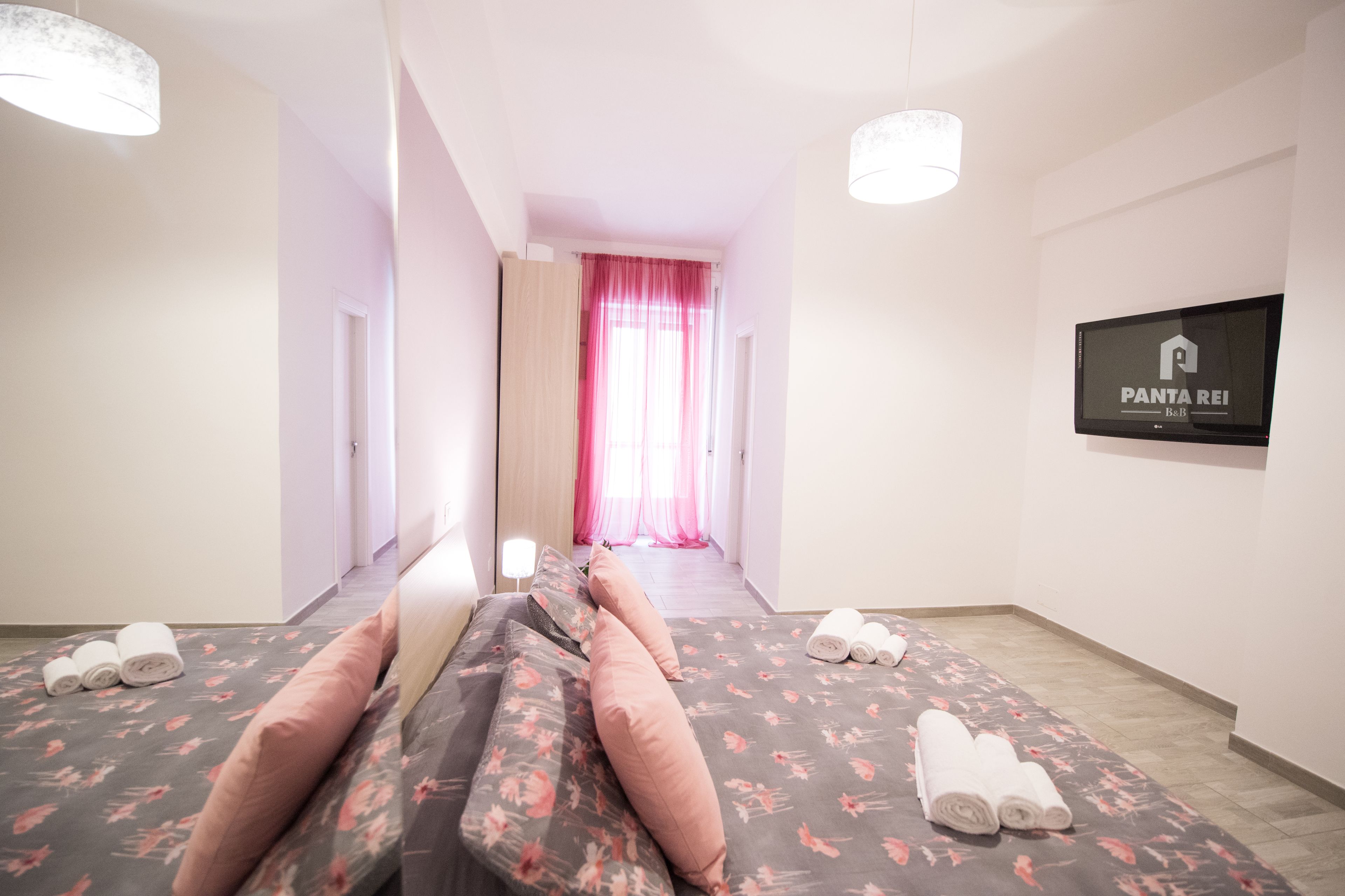 Una habitación de hotel con cama, televisión y un pasillo que lleva a un baño.