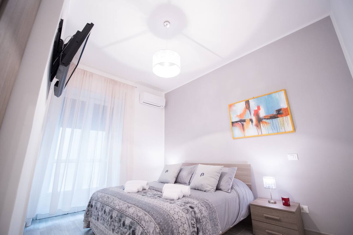 A bedroom with a bed, bedside table, and a painting on the wall.