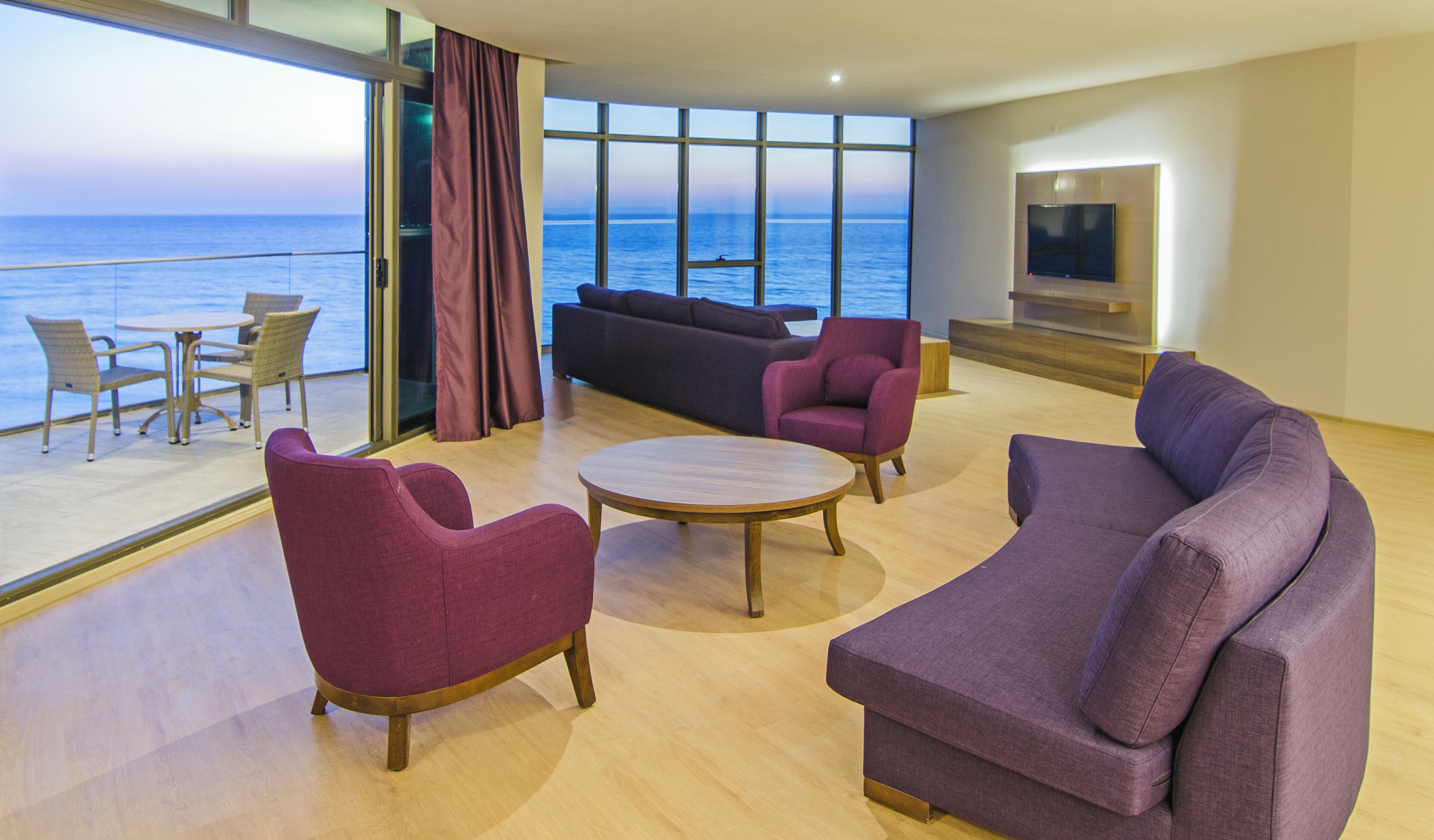 Un salon moderne doté d’une grande fenêtre donnant sur la mer, meublé de canapés violets et d’une table basse ronde.