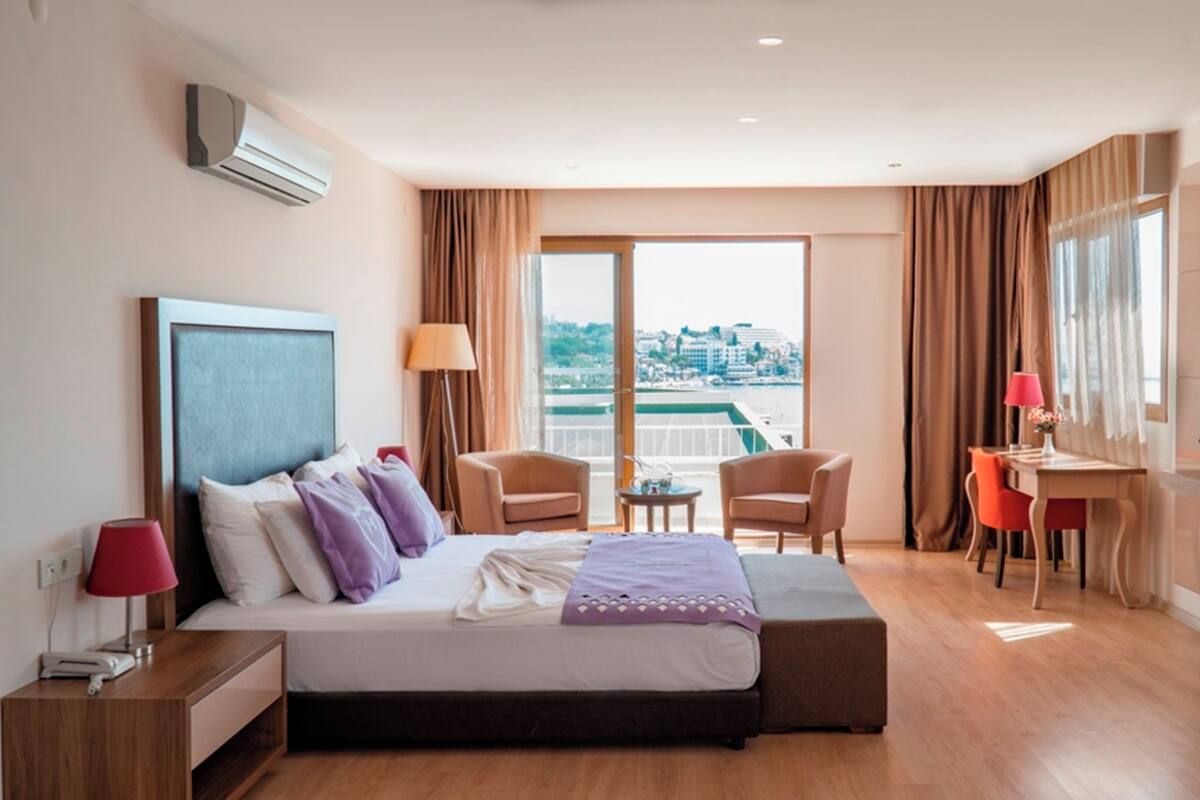 Habitación de hotel con una cama grande, un escritorio, dos sillas, un televisor y vista a la ciudad.