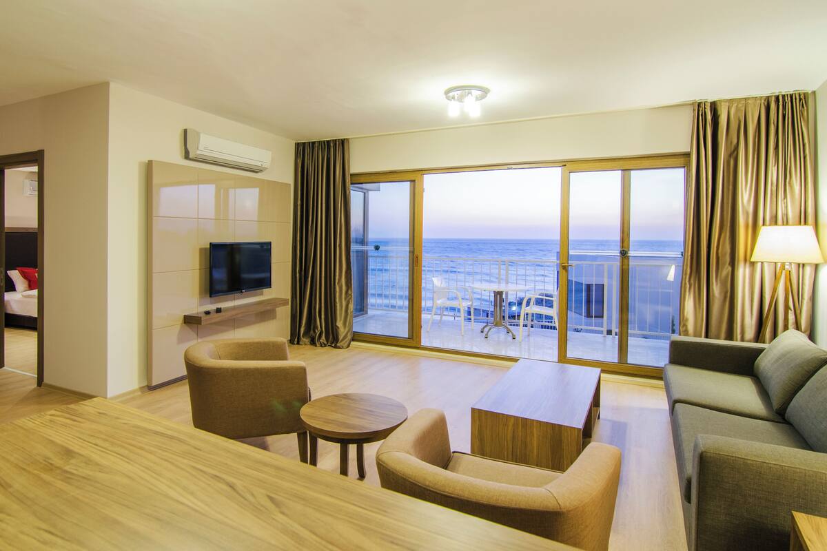 Habitación de hotel con balcón, televisor, sofá, mesa y silla.