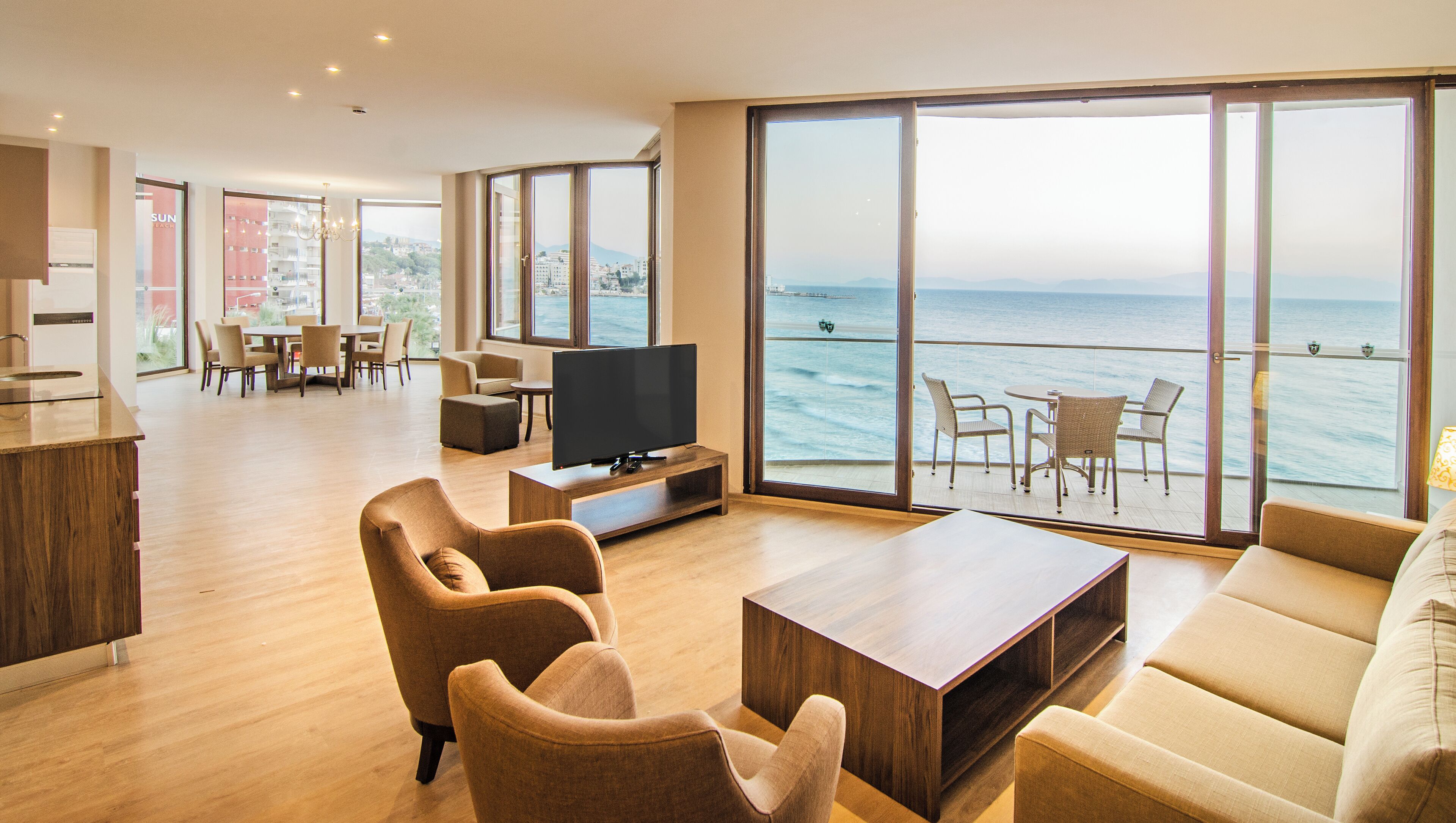 Un vaste espace de vie comprenant un grand téléviseur, des sièges confortables, un coin repas et un balcon avec vue sur la mer.