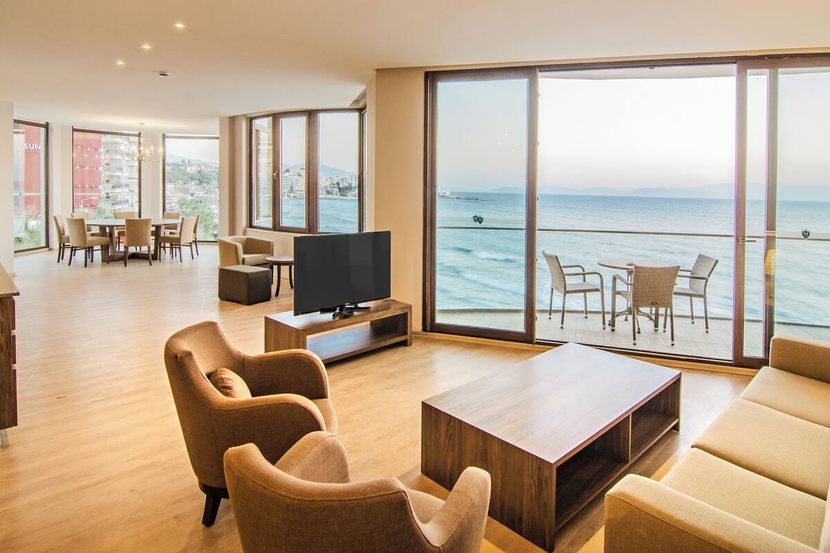 Amplia sala de estar con televisor grande, asientos cómodos y vista al mar.