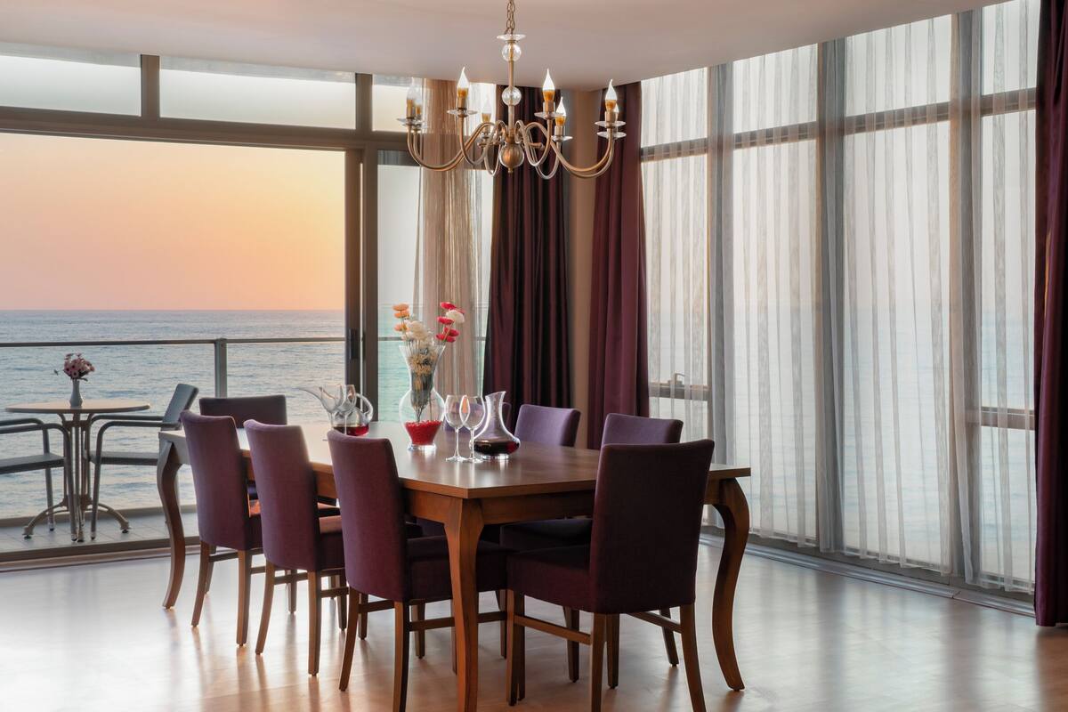 Comedor con vista al océano, un candelabro y una mesa preparada para seis personas.