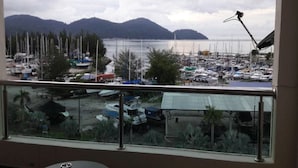 A view from a balcony overlooking a marina with boats and mountains in the background. - Marina Island Apartment (Lumut)