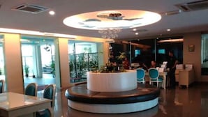 A modern lobby with a central circular seating area, a reception desk, and a large window providing a view of the outdoors. - Marina Island Apartment (Lumut)
