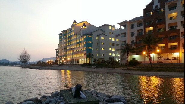 A hotel with multiple floors, a pool, and a rocky area with a person sitting. - Marina Island Apartment (Lumut)