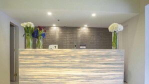 A reception desk with a marble top, two vases with flowers, and a tiled wall behind. - Ramada Encore Makati (Makati City)