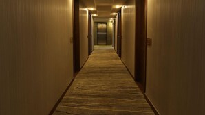 A hotel hallway with carpeted floors, wooden doors, and a central elevator. - Ramada Encore Makati (Makati City)