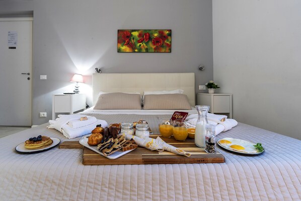 Una cama bien hecha con una bandeja de desayuno, que incluye panqueques, pasteles y jugo de naranja, en una habitación de hotel con un cuadro en la pared.