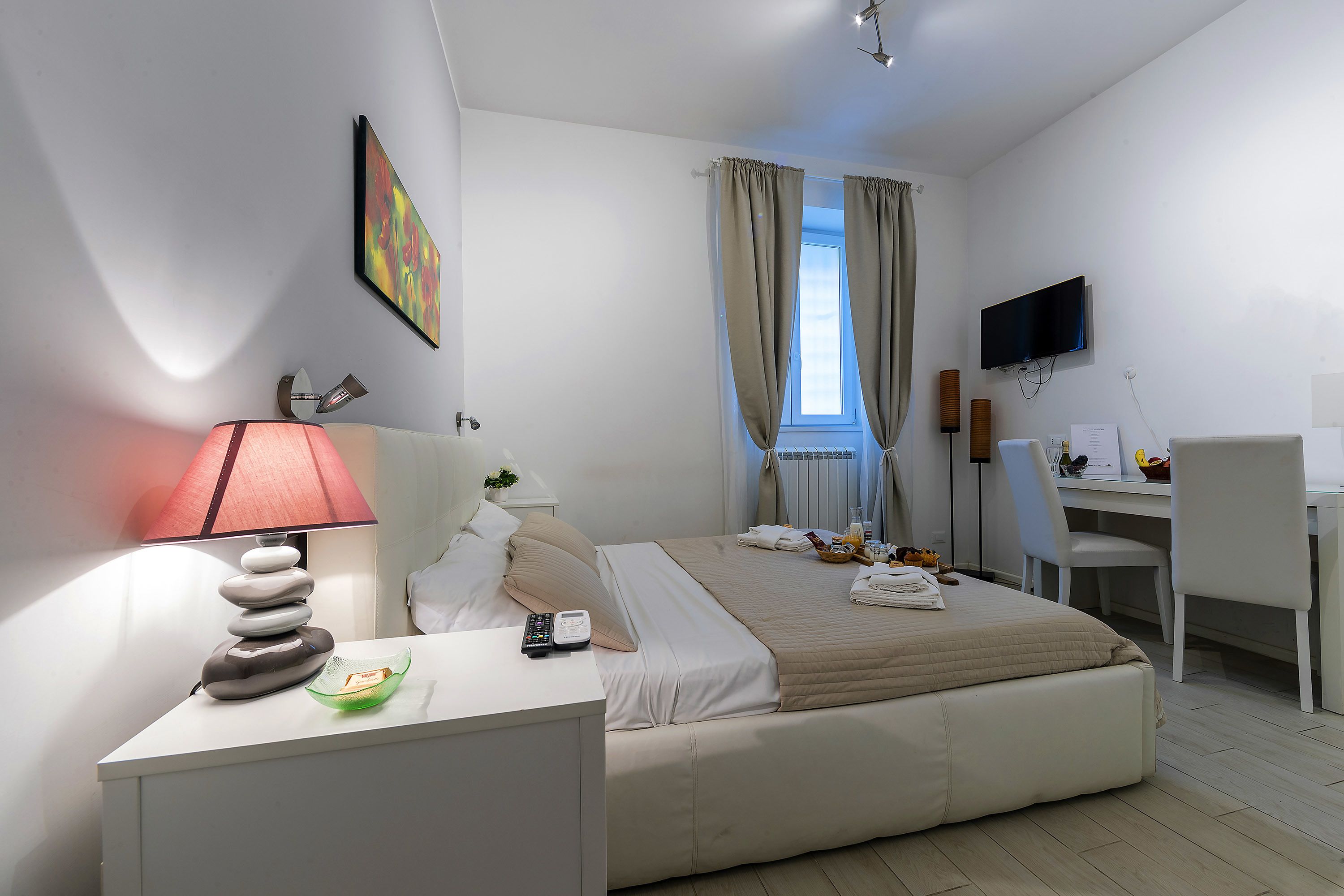 A modern hotel room with a bed, desk, and chair, a flat-screen TV, and a window with curtains.