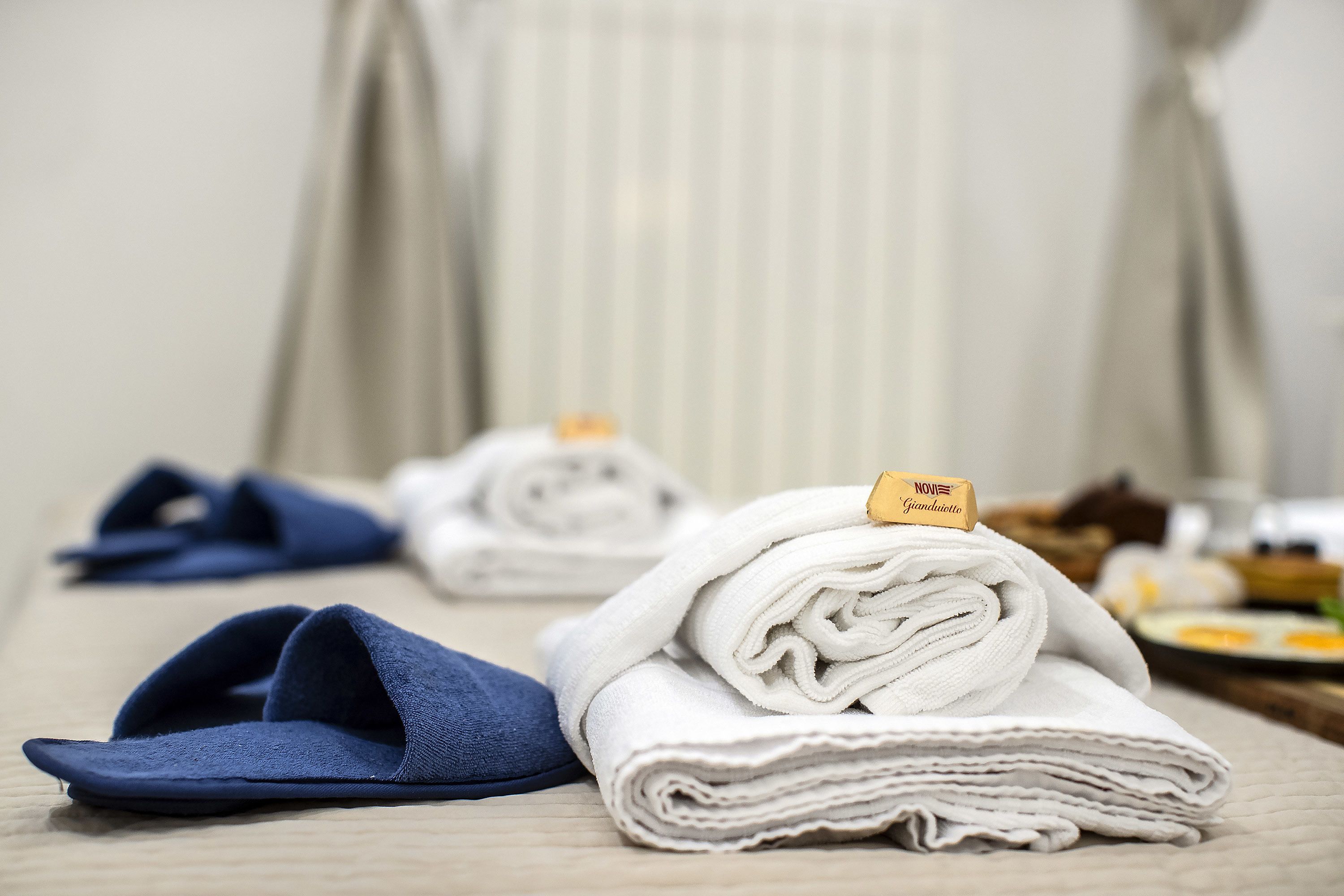 Una habitación de hotel ordenada con una cama, una toalla doblada y un par de zapatillas.