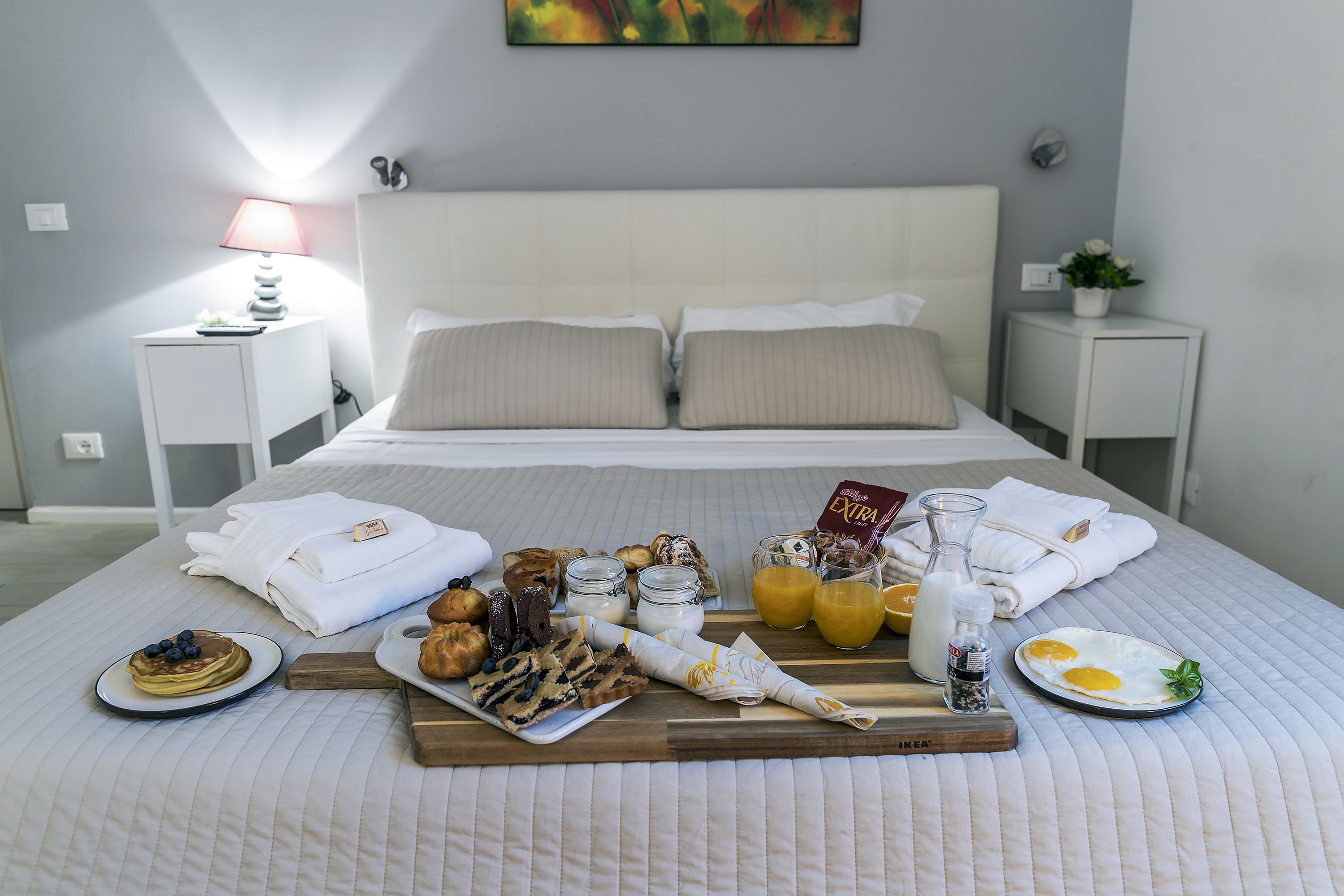 A neatly made bed with a breakfast tray, pillows, and a bedside table with a lamp.