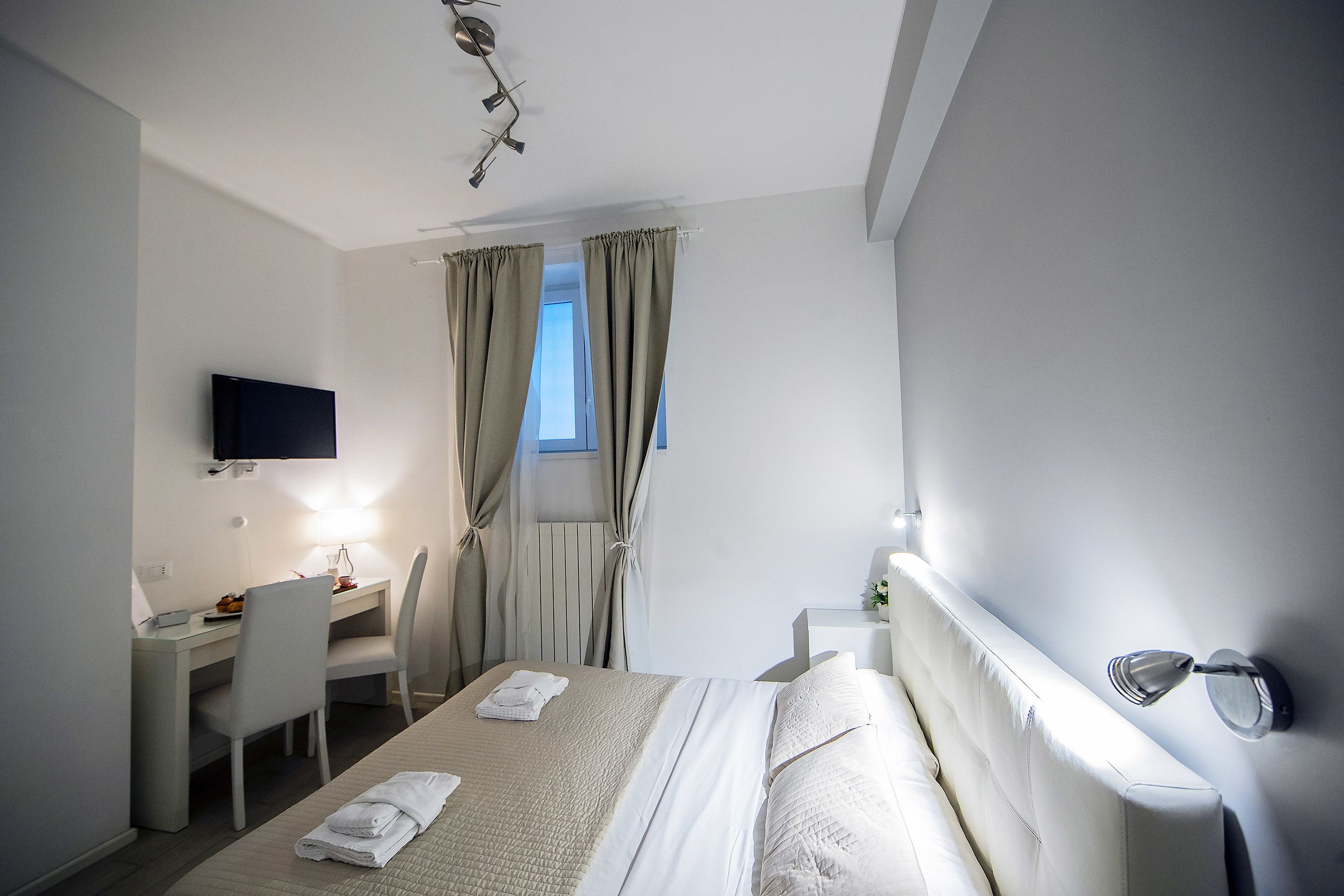 Una camera d'albergo con un letto, una scrivania, una sedia, una televisione e tende.