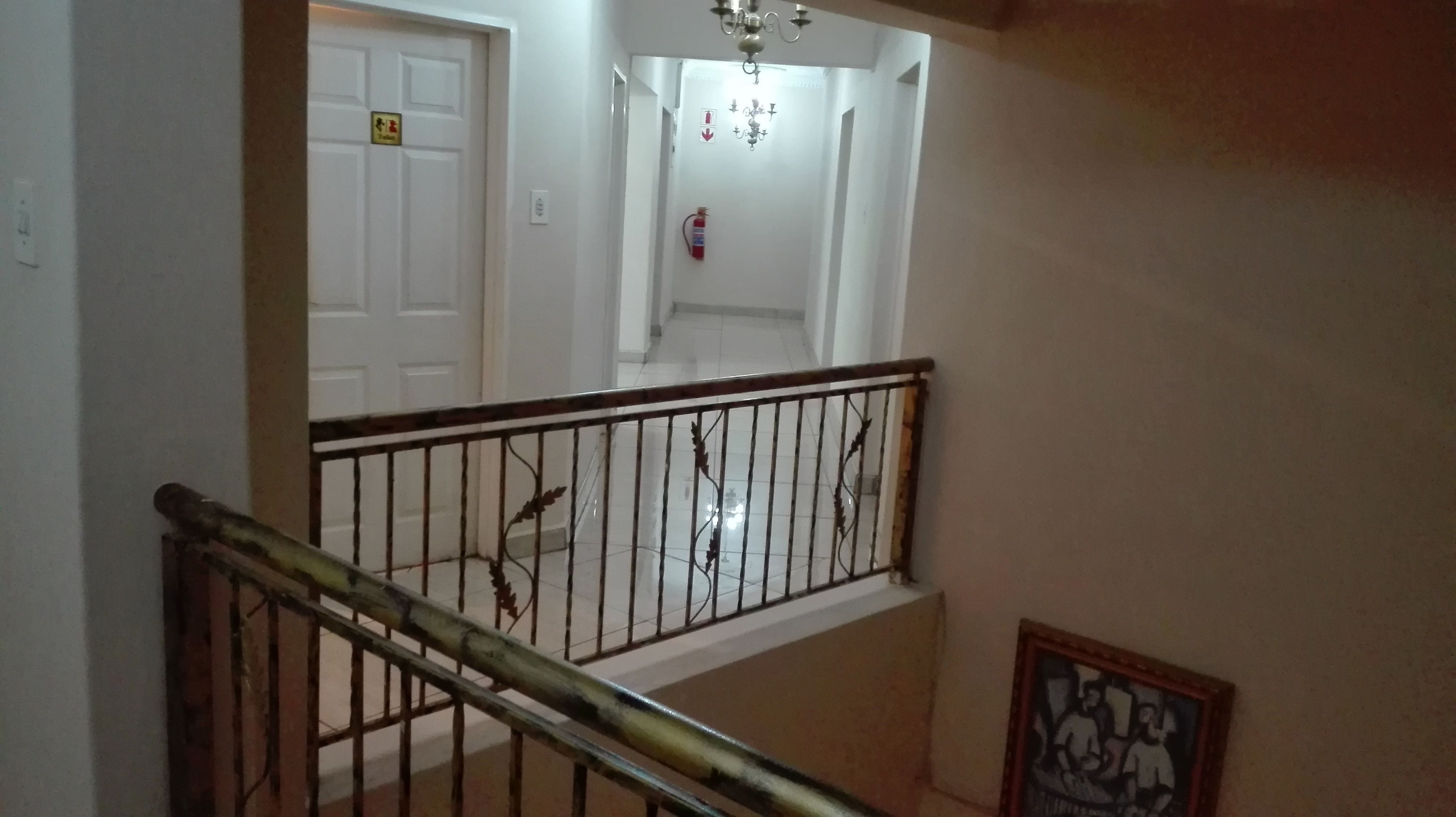 Uma escada com corrimão de metal, um extintor fixado na parede e uma porta com uma placa acima.