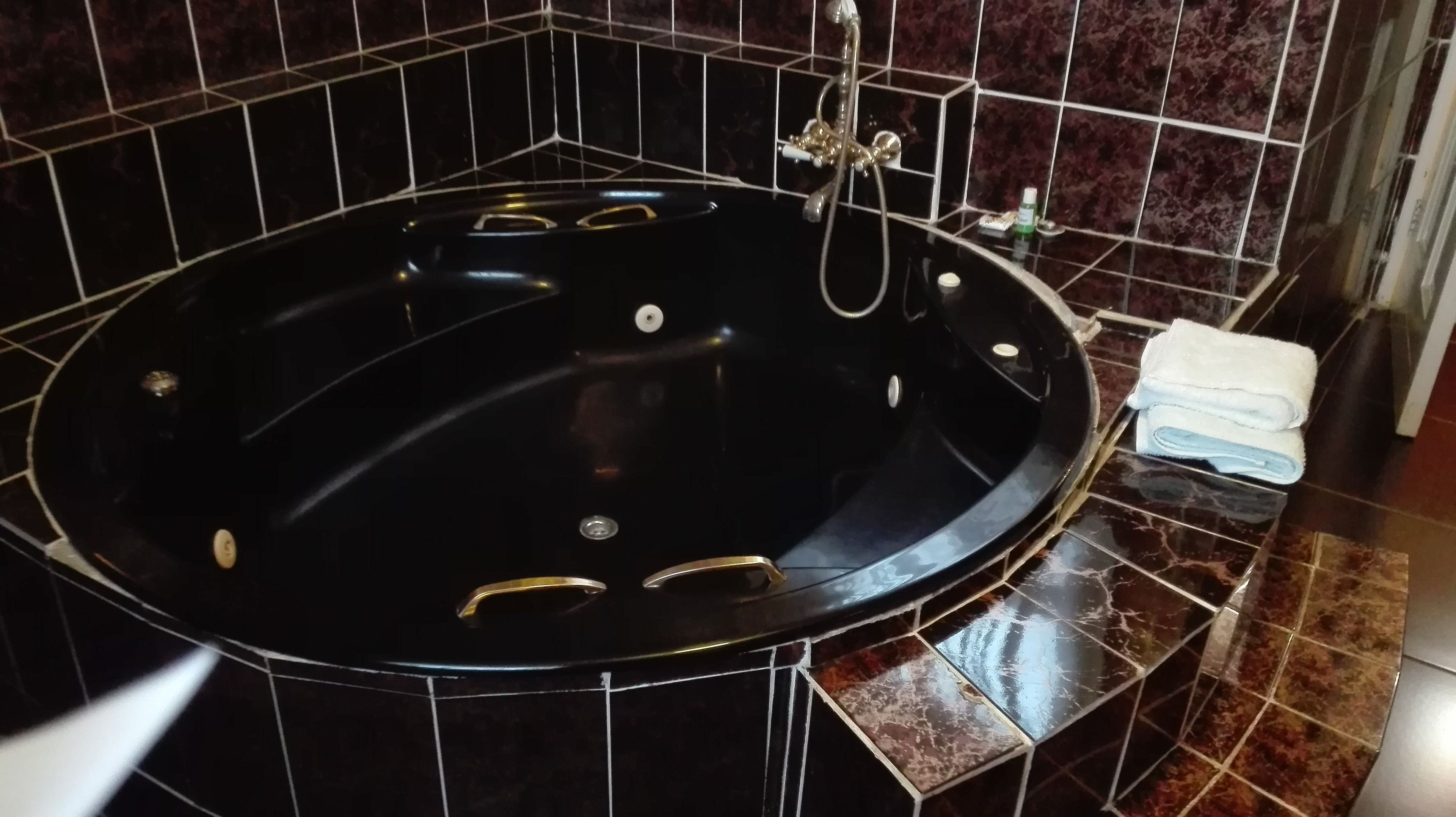 A black jacuzzi tub with gold handles, set against dark tiled walls.