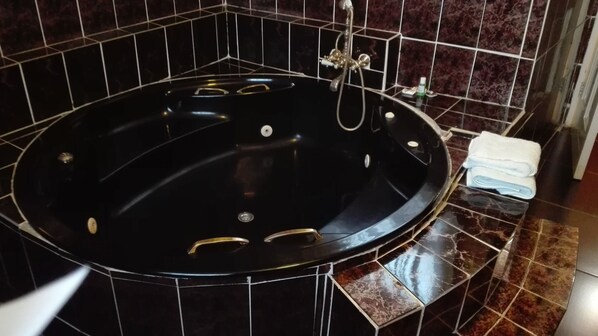 A black jacuzzi tub with gold handles, set against dark tiled walls. - Lapeng Village (Benoni)