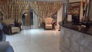 A living room with a sofa, a chair, a tiled floor, and a kitchen counter.