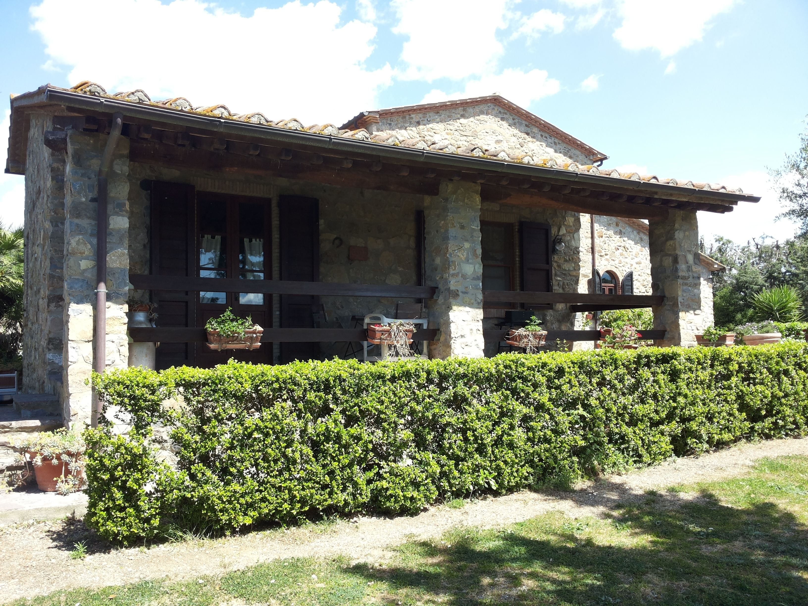 A stone building with a tiled roof, wooden porch, and potted plants.