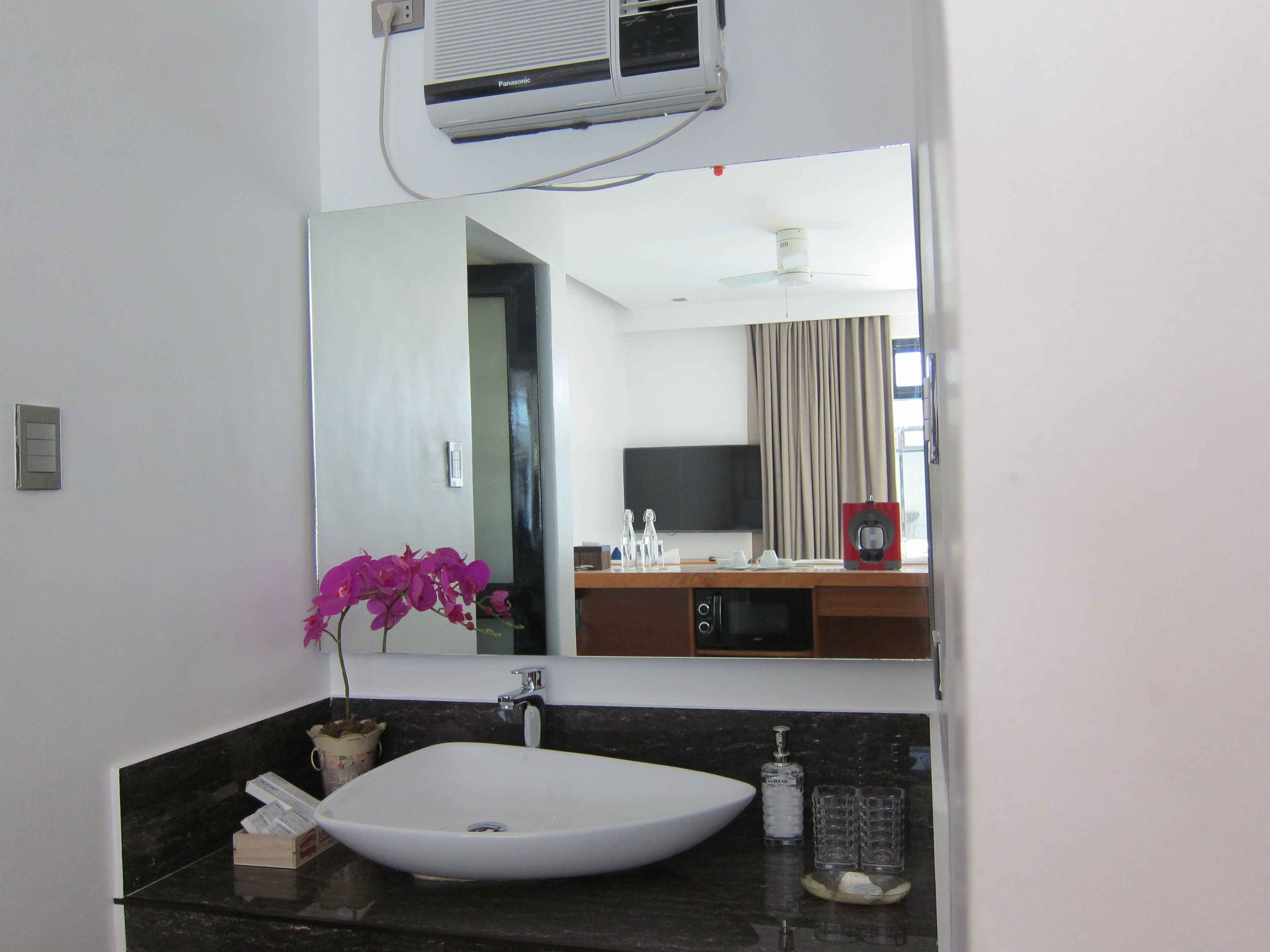 A bathroom with a white sink, a mirror, a purple orchid, a bottle of hand soap, and a ceiling fan.