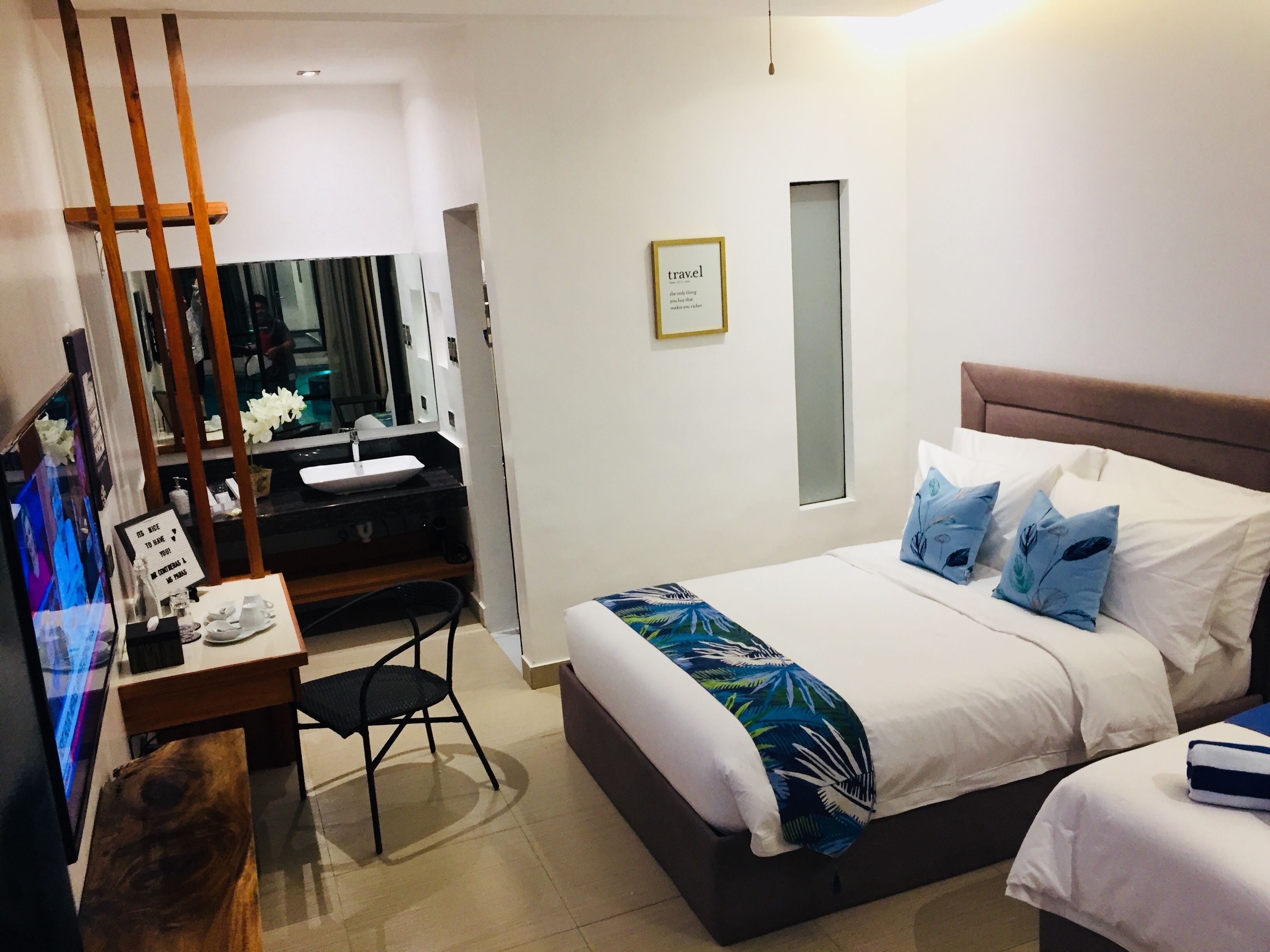A modern hotel room with a bed, bedside table, and a desk with a chair.