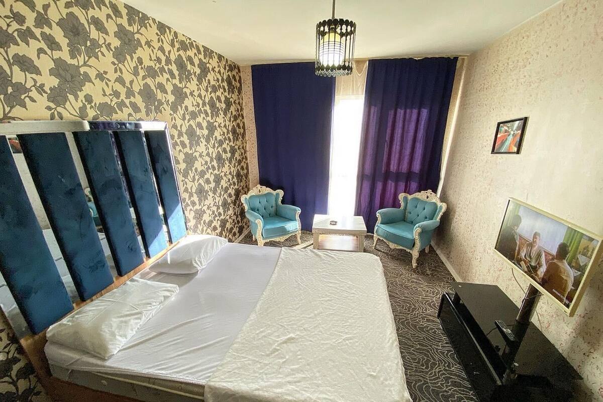 Habitación de hotel con una cama grande, dos sillones, una mesita, un televisor y una alfombra estampada.