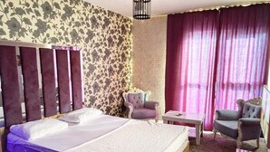 A bedroom with a large bed, two armchairs, a small table, and a patterned wall. - King Suit Konaklama (Istanbul)