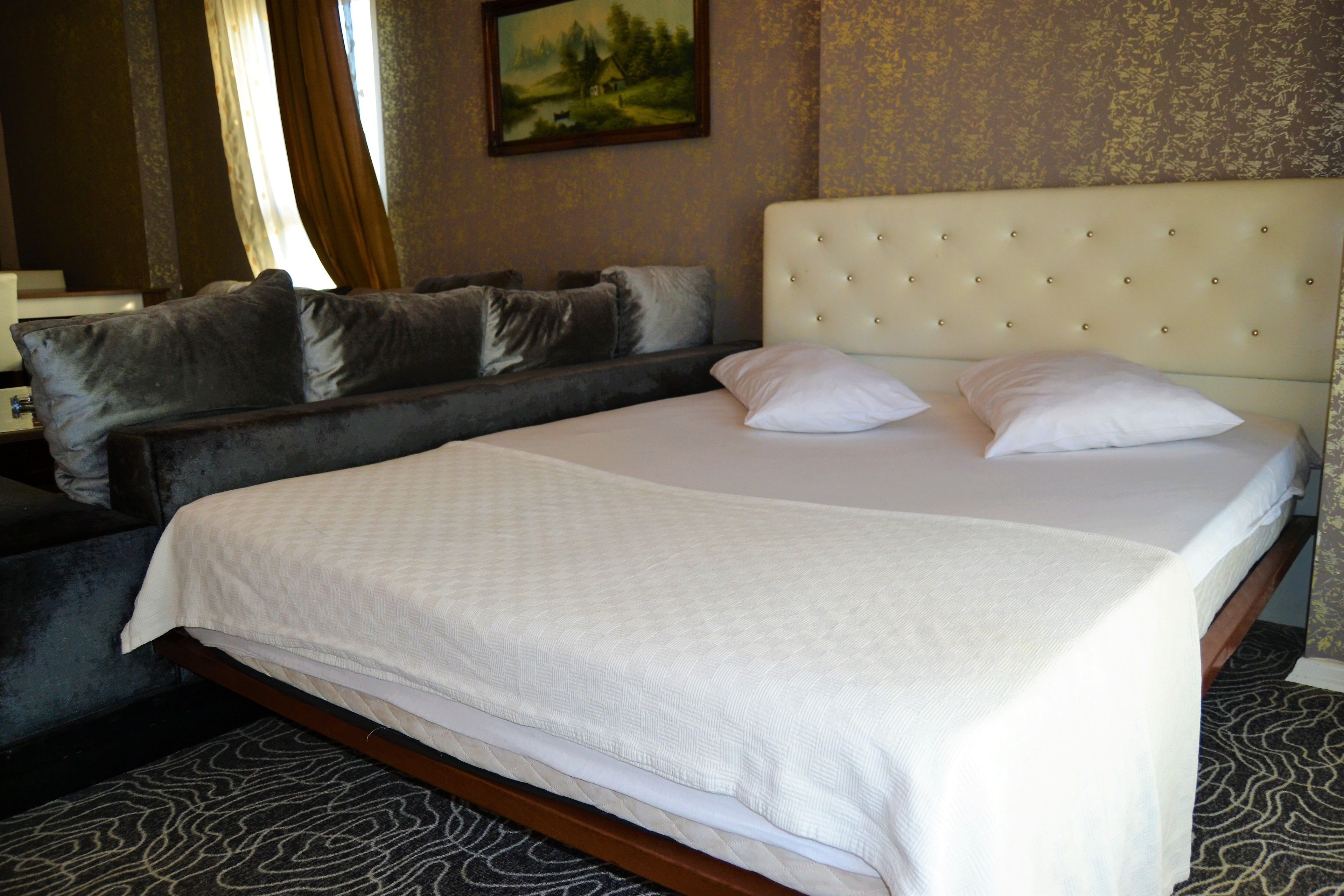 A hotel room with a large bed, a sofa, and a painting on the wall.