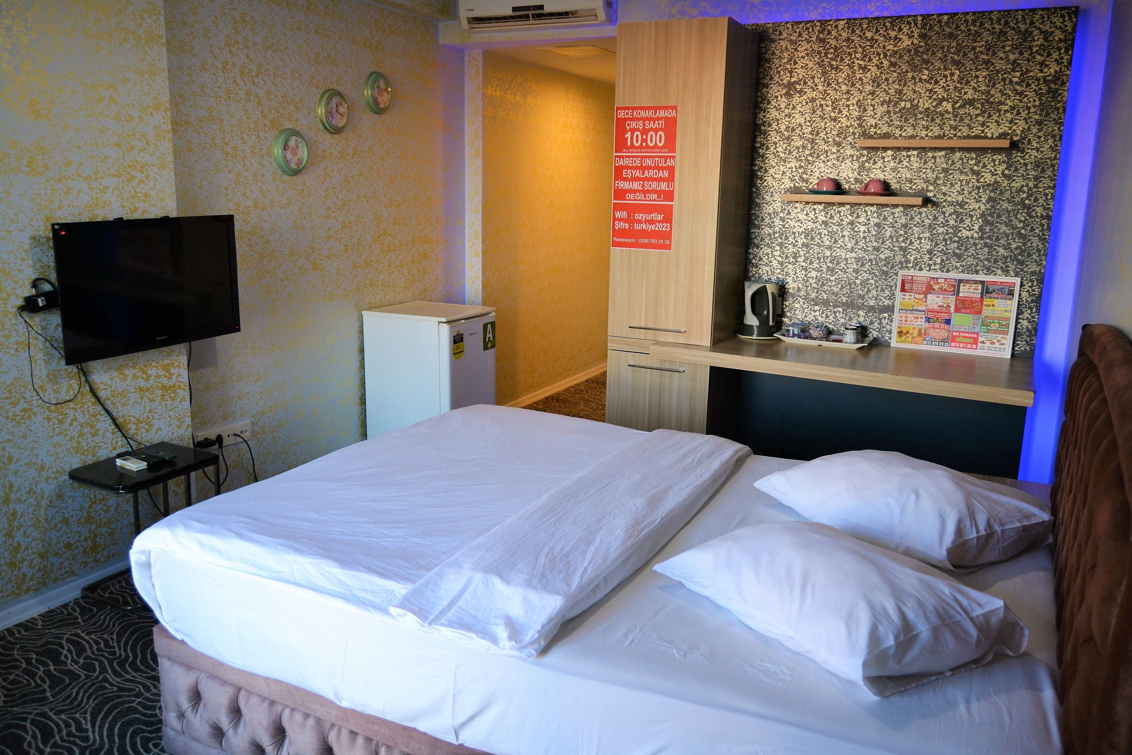 Een hotelkamer met een bed, een televisie, een kleine koelkast, een wastafel en een spiegel.